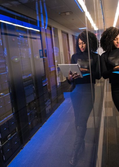 A woman using a laptop navigating a contemporary data center with mirrored servers.
